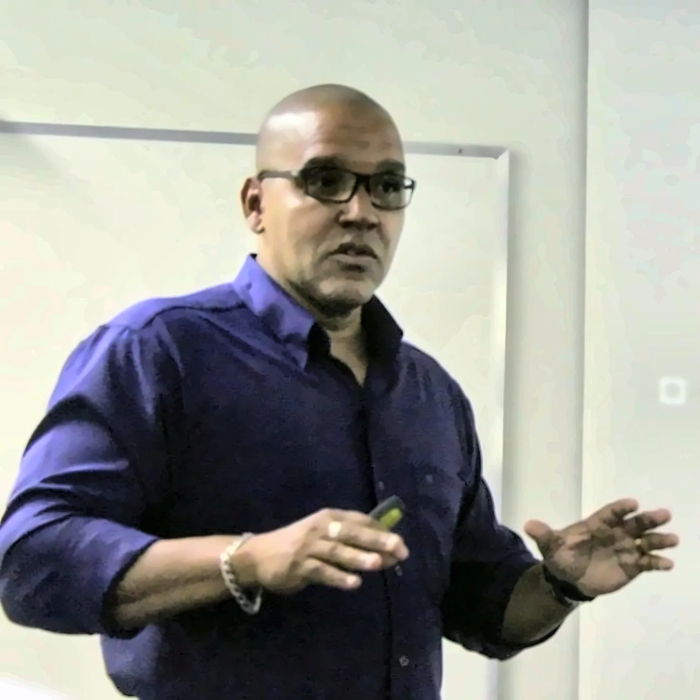 Luetil Neto fala em sala, de camisa azul escura